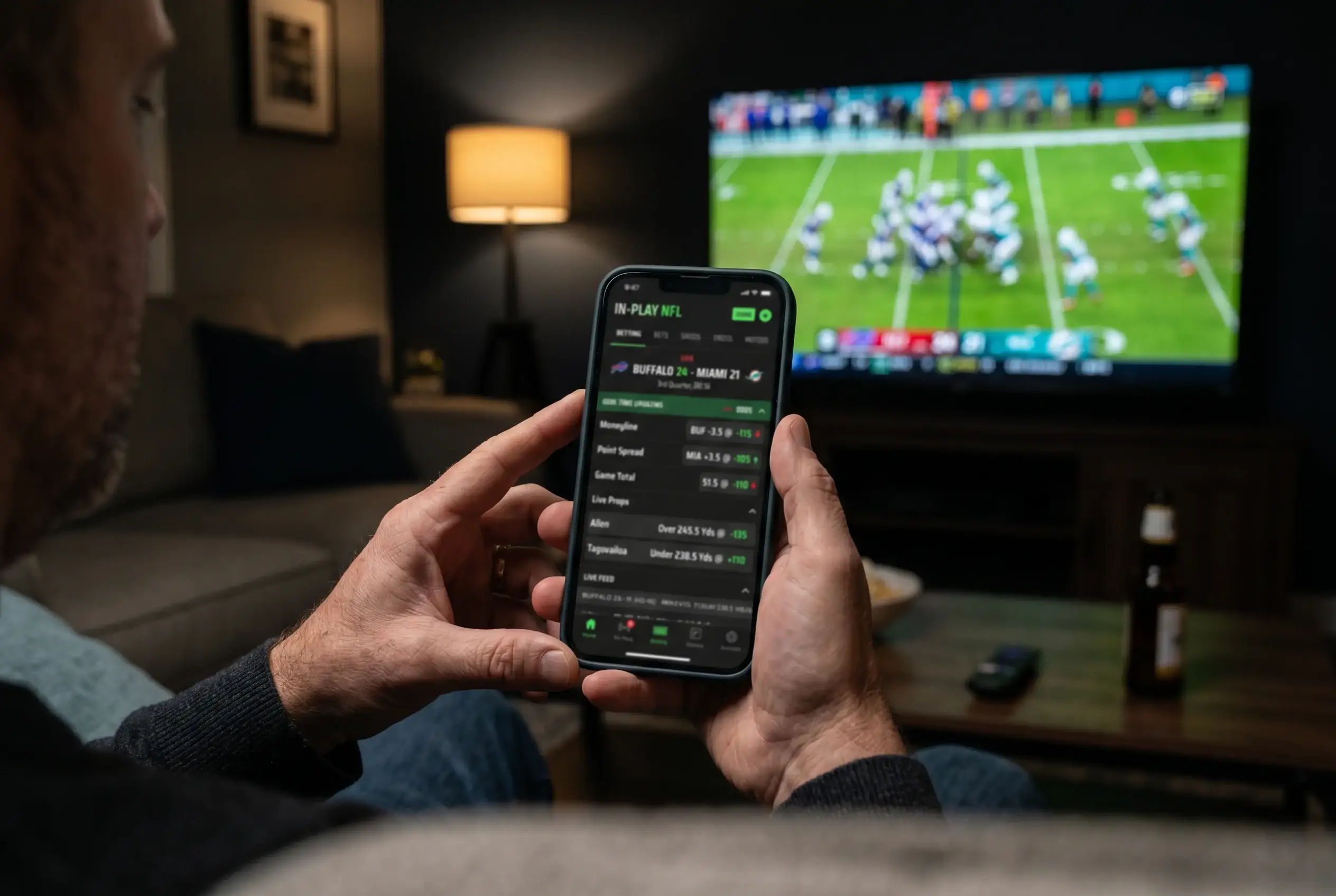 Close-up of a person watching an NFL game on television while placing an in-play bet on a mobile phone